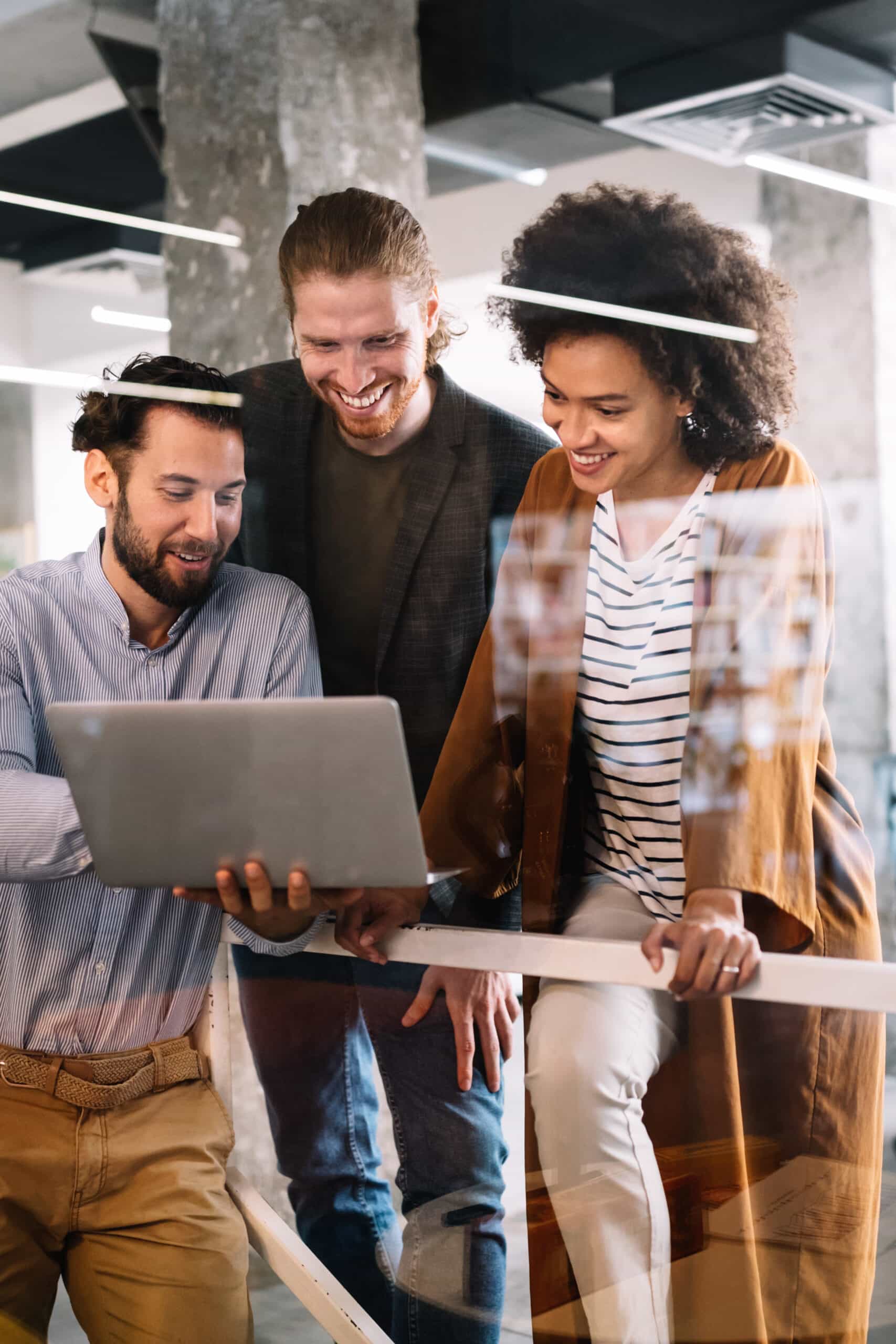 3 young professionals smiling while pointing at a laptop.