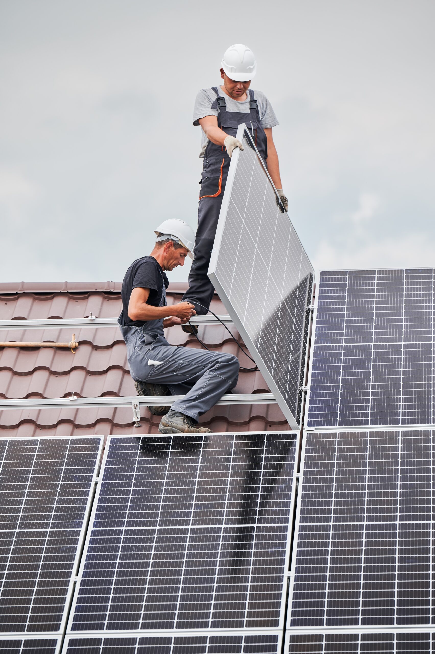 Two technicians on a roof installing solar panels.