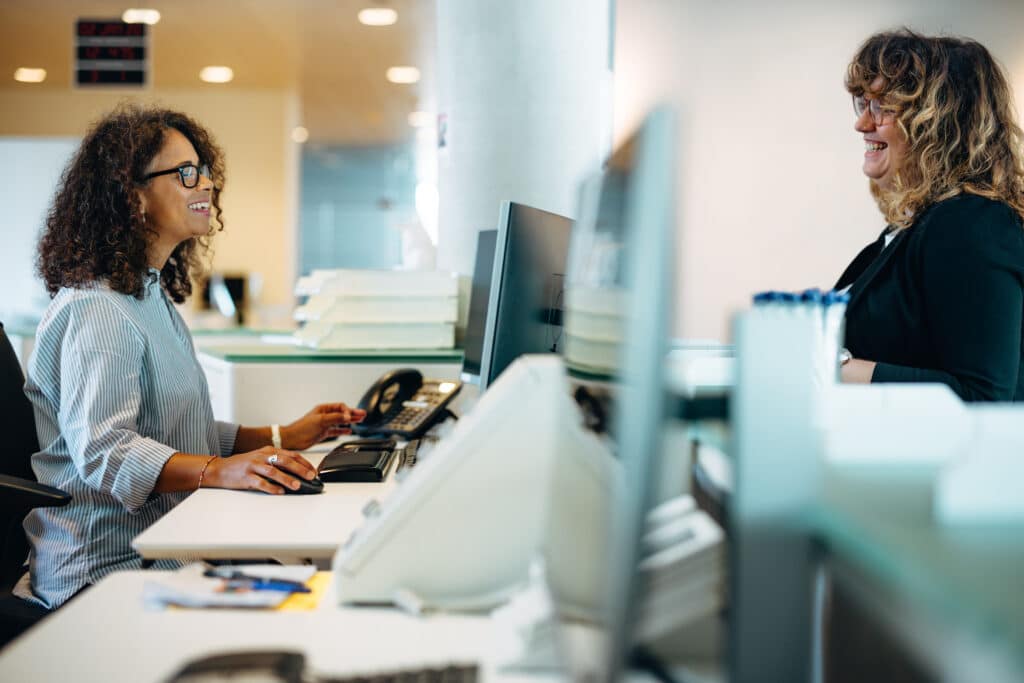 Two administrators smiling at each other over a row of computer screens.